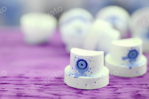 Preview: The soiled blue nozzles from the paint sprayer lies on a purple plank on a background