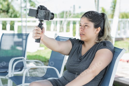 Preview: young latina woman blogger, sitting on a chair making a video of herself for her social networks.