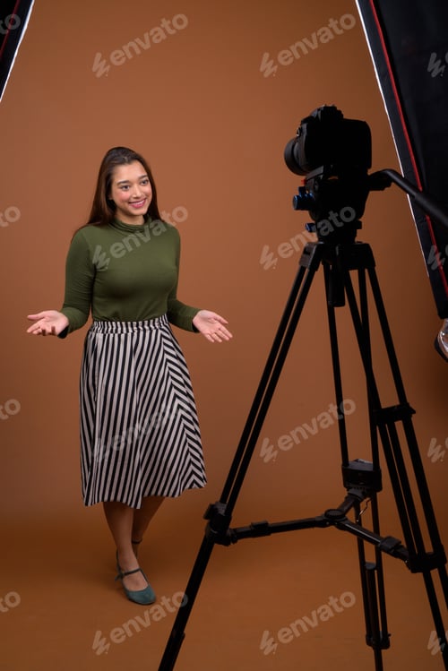 Preview: Young beautiful Indian woman vlogging against brown background