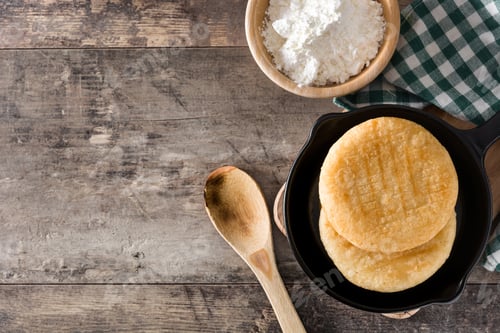 Preview: Delicious arepas in frying pan with precooked corn flour on rustic wooden table