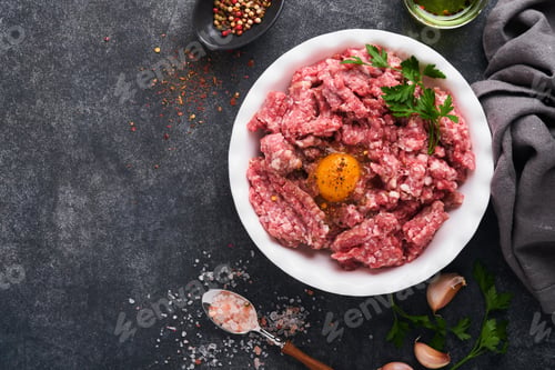 Preview: Raw minced meat. Ground meat beef, pork or lamb spices, herbs and eggs on white plate on black old c