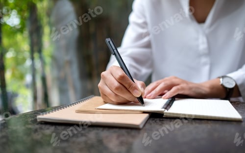 Preview: Closeup image of a woman writing on a notebook on the table