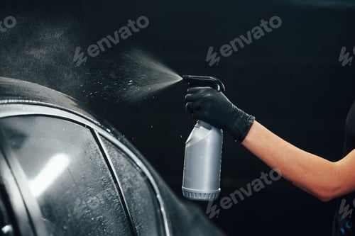 Preview: Spraying the vehicle. Modern black automobile get cleaned by woman inside of car wash station