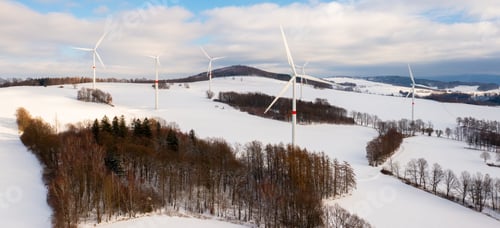 Preview: Wind turbine on winter field against cloudy blue sky during sunset.