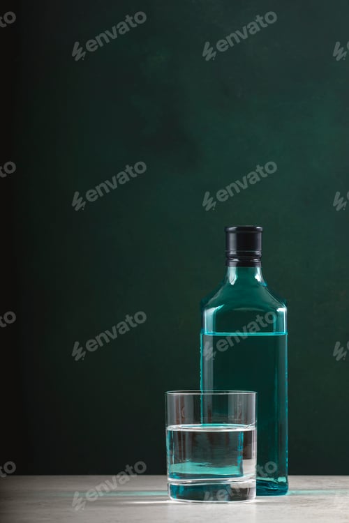 Preview: Dry gin in glass with sapphire blue bottle on dark green background