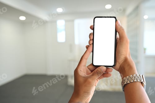 Preview: Woman hands holding smart phone over blurred bright living room background.