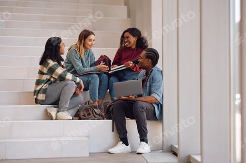 Preview: Happy university friends talking while relaxing on stairs in a hallway.