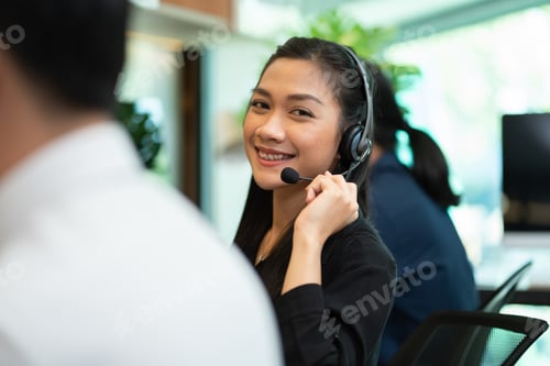Preview: Asian female telemarketing agent wearing microphone headset talking with customer