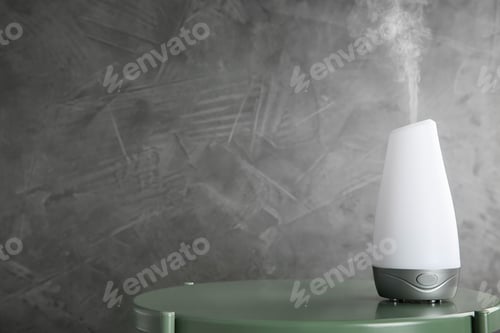 Preview: Modern essential oil diffuser on green table against dark grey background. Space for text