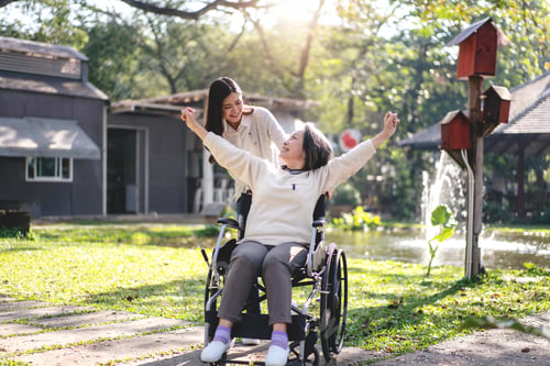 Preview: Young asian woman pushing wheelchair of mother to relaxation in the garden while senior woman