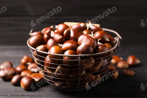 Preview: Fresh sweet edible chestnuts in basket on black table, closeup