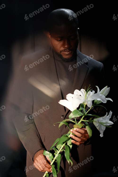 Preview: Shot with Ghost Glare of Black man Holding Flower in Spotlight in Dark Studio