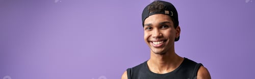 Preview: Transgender smiling man with mobile in hand on purple background. Cheerful male in casual dress