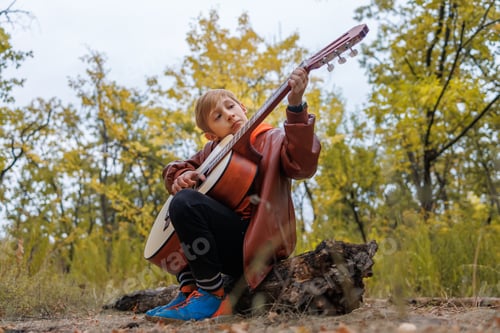 Preview: in autumn in the park a boy plays the guitar looks at the strings and tunes the guitar