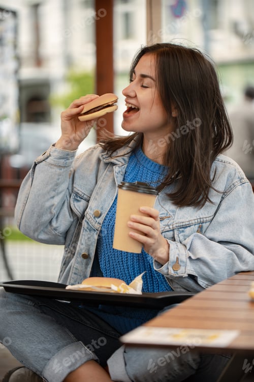 Preview: Street portrait of cheerful young woman eating fast food.
