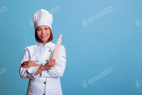 Preview: Cheerful smiling cook standing with arm crossed holding kitchen rolling pin