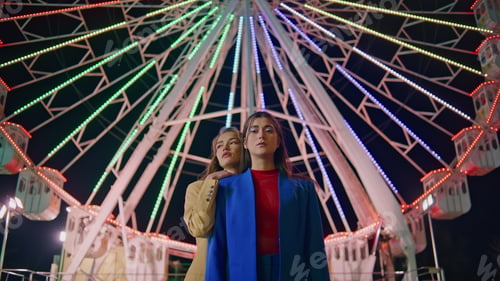 Preview: Girlfriends posing ferris wheel at night. Two models resting illuminated funfair