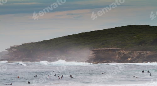 Preview: Winter surfers in the ocean waiting for a wave, with green cliffs in background