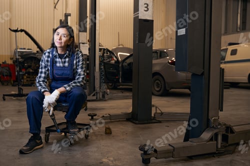 Preview: Joyous lady in overalls resting on chair at repair shop