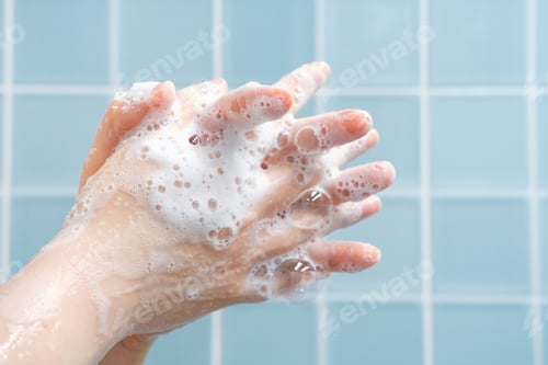 Preview: The woman washes her hands with foam against blue tiles background in bathroom side view close-up.