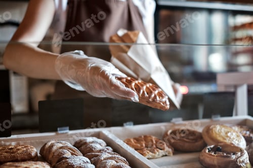 Preview: European woman sells in bakery putting bread in paper bag.