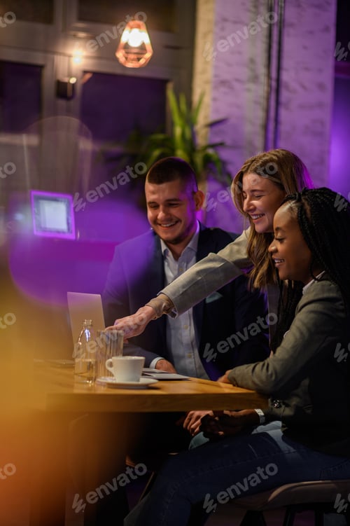Preview: Cheerful work colleagues working on a laptop while having a meeting in a cafe