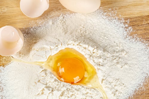 Preview: Closeup of a cracked egg on a pile of flour on a wooden surface
