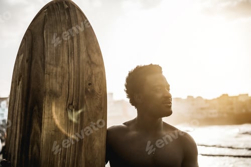 Preview: African surfer man holding vintage surf board on the beach at sunset - Soft focus on face