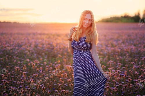 Preview: portrait of a beautiful young girl in a flower field at sunset in the countryside in spring (summer)