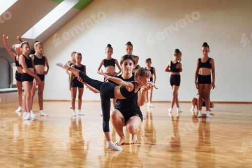 Preview: With help from coach. Group of female kids practicing athletic exercises together indoors