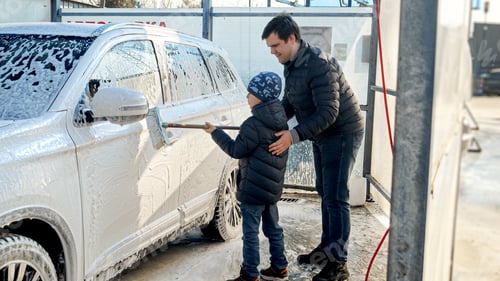 Preview: Young father teaching his little son wshing car at self service cash wash