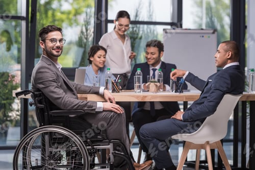 Preview: selective focus of smiling disabled businessman looking at camera while colleagues discussing work