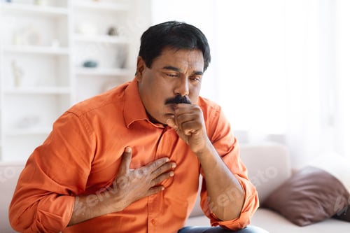 Preview: Unhealthy sick indian middle aged man coughing, home interior
