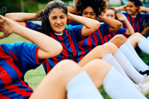 Preview: Women's soccer team practicing sit-ups during sports training on playing field.