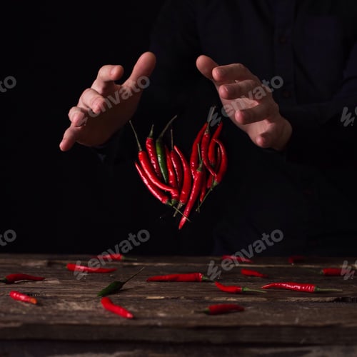 Preview: Hot Red Chili Peppers Arranged with Hands on Table
