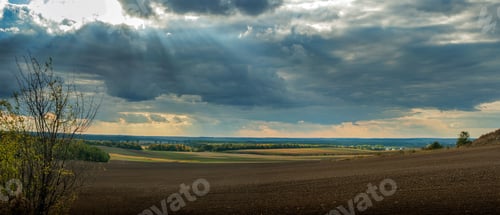 Preview: panorama of plowed land with fields, forests on the horizon, sun rays through the dark sky