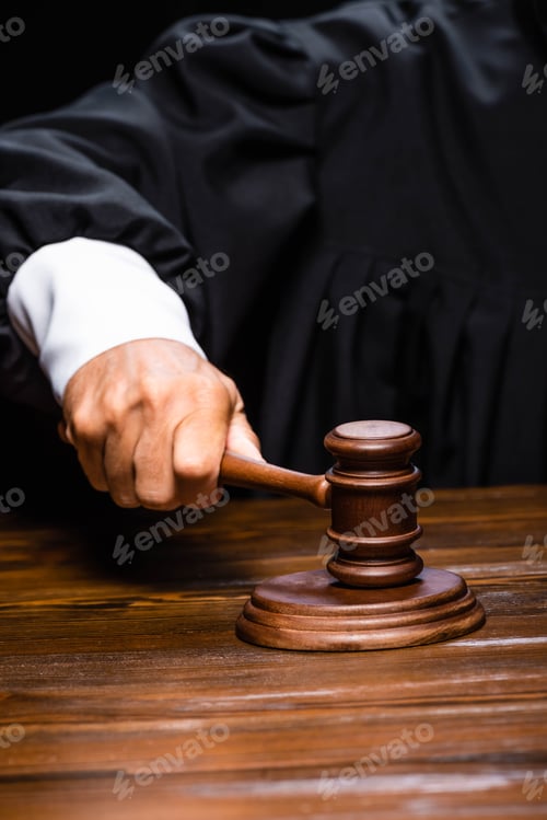 Preview: cropped view of judge in judicial robe sitting at table and hitting with gavel isolated on black
