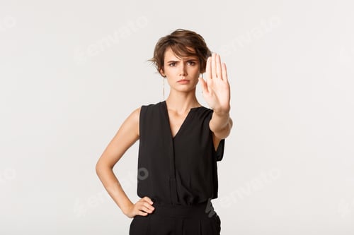 Preview: Young serious woman tell to stop, say no, extend hand as showing prohibition gesture, standing over