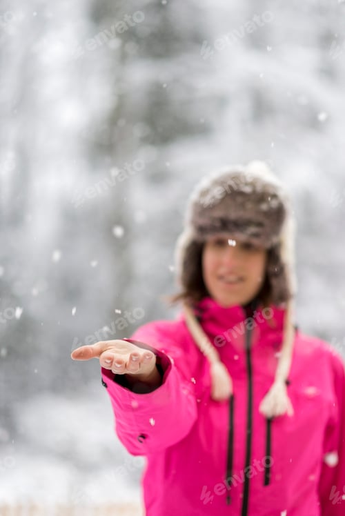 Preview: Young woman standing in a snow extending her arm in front of her to catch snow flakes