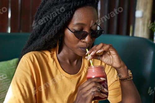 Preview: Young woman with dreadlocks drinking a smoothie in a cafe