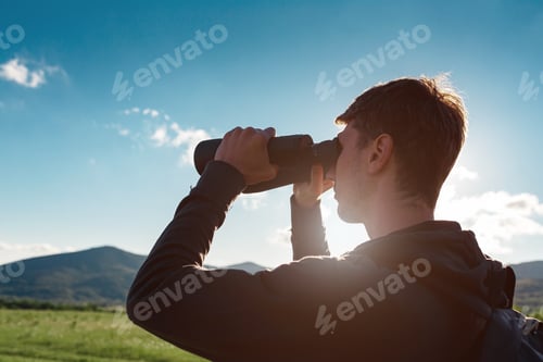 Preview: Young man at mountain looking through binoculars