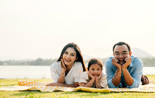 Preview: Asian family father mother and daughter lying on blanket spring meadow field grass in park cheerful