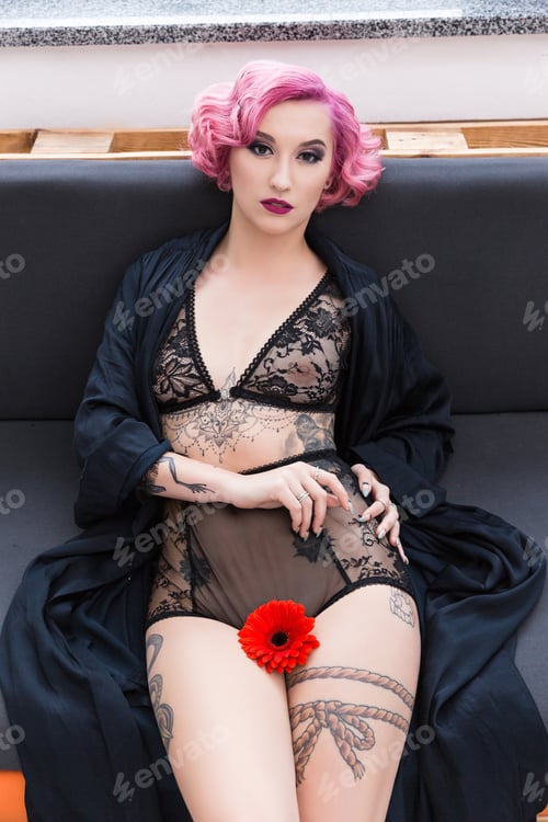 Preview: seductive tattoed pin up girl in transparent lingerie with flower posing on couch