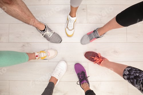 Preview: Closeup of athletes wearing sports shoes and standing in circle on wooden floor, top view