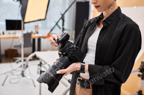 Preview: cropped view of young female photographer in everyday attire working in her studio with equipment