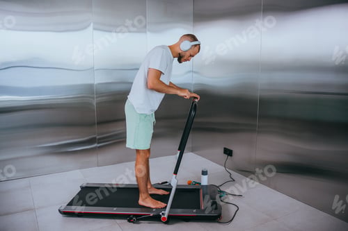 Preview: Man in casual enjoying music on headphones while walking on a treadmill, in a sleek, modern space