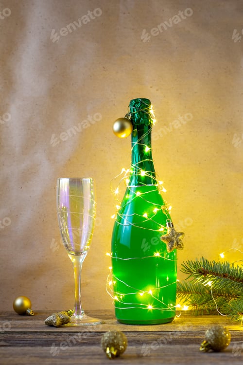 Visualização: uma garrafa de champanhe verde embrulhada em uma guirlanda brilhante como uma árvore de Natal e um copo. Ano novo