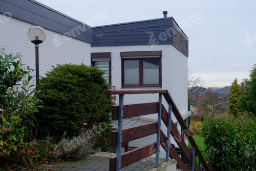 Preview: Modern house surrounded by greenery under the cloudy sky with a village on the background