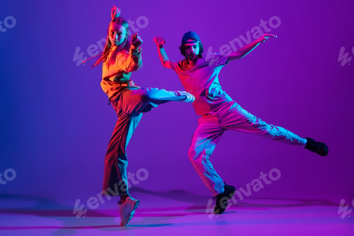 Preview: Two dancers, young man and woman dancing hip-hop in casual sports youth clothes on gradient purple