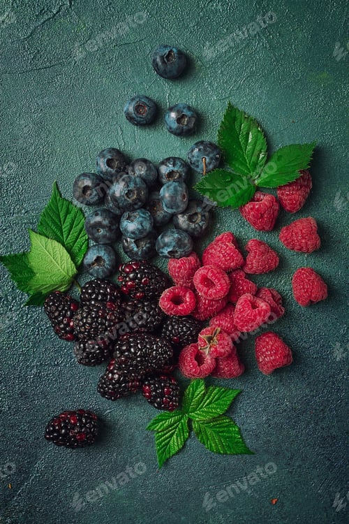 Preview: a mix of ripe berries, with leaves scattered on the table, raspberries, blackberries, blueberries,